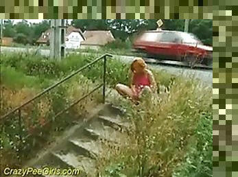 Girl takes a piss next to a public street