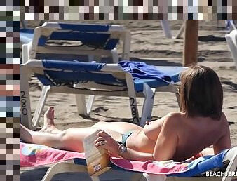 Topless leggy milf reads magazines at the beach